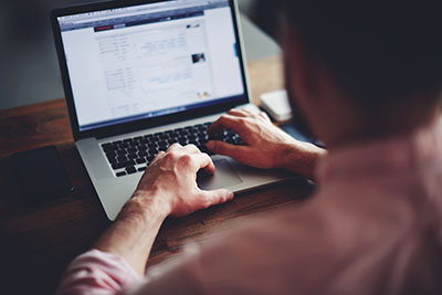 Man sitting at desk while typing on his laptop.