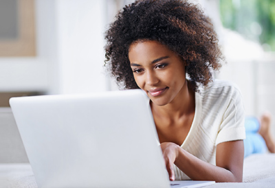 Image of woman lounging on bed looking at her laptop.